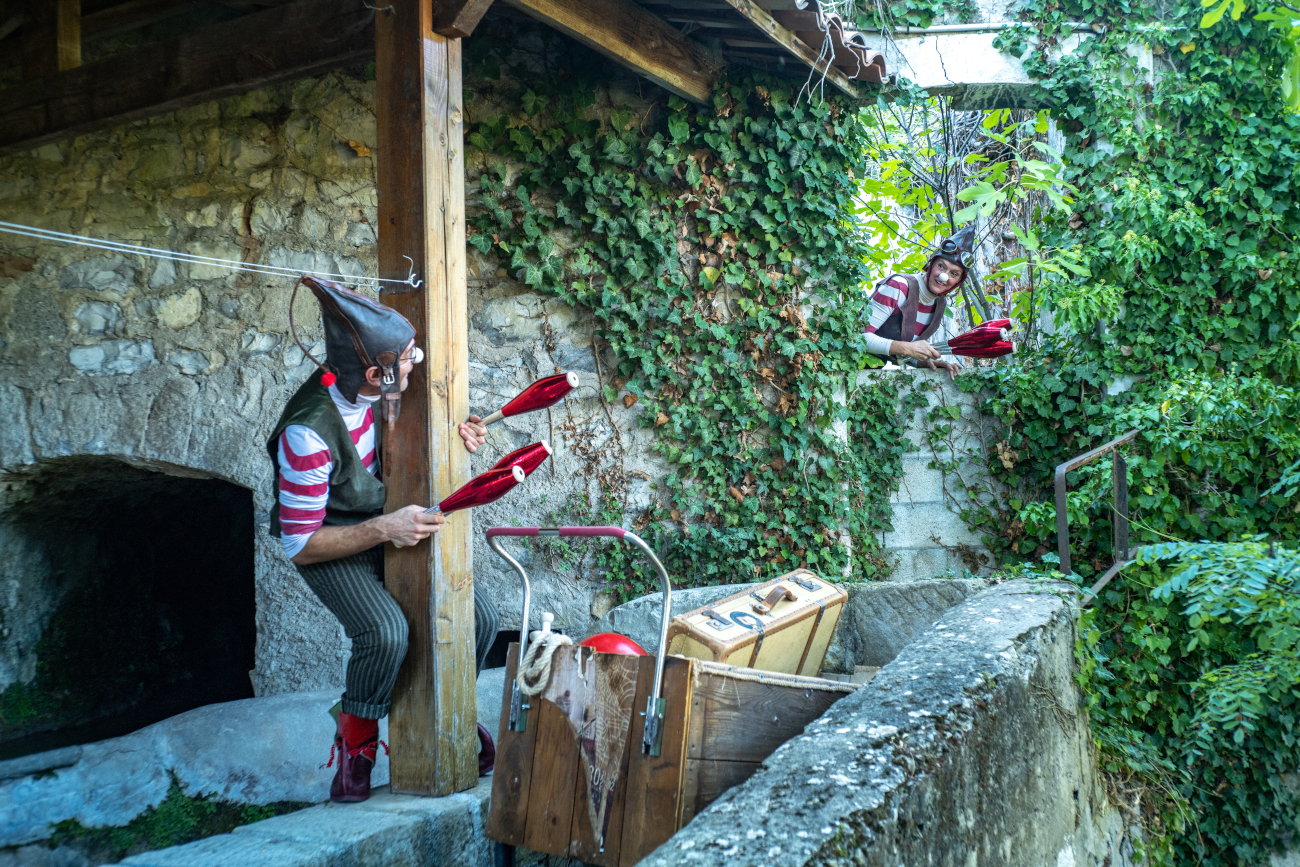 Dans une rue sous un arche à Villars sur Var, 2 lutins Circassiens jongle avec des balles lumineuses multicolores. les lutin portent un nez de clown blanc.